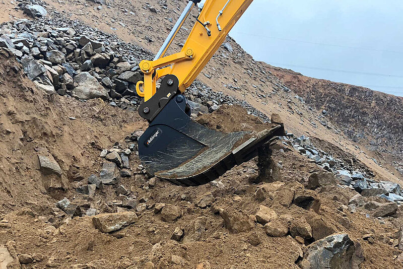 Standard Backhoe Bucket (11 to 40 t) by Rädlinger filled with soil and pieces of rock