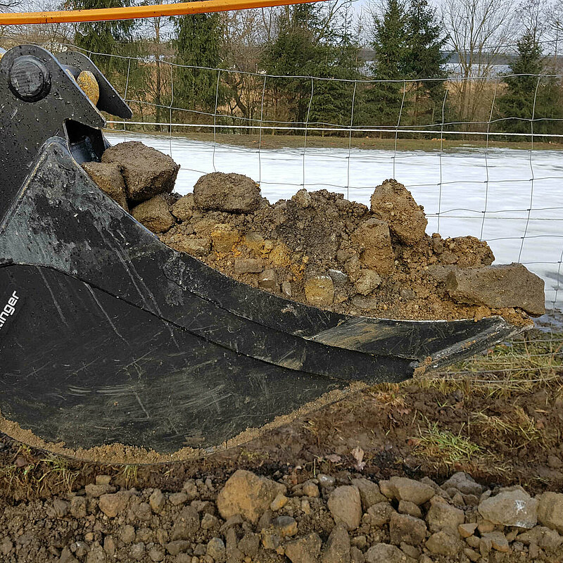 Close-up of a Standard Backhoe Bucket without Teeth (up to 6 t) by Rädlinger, filled with soil
