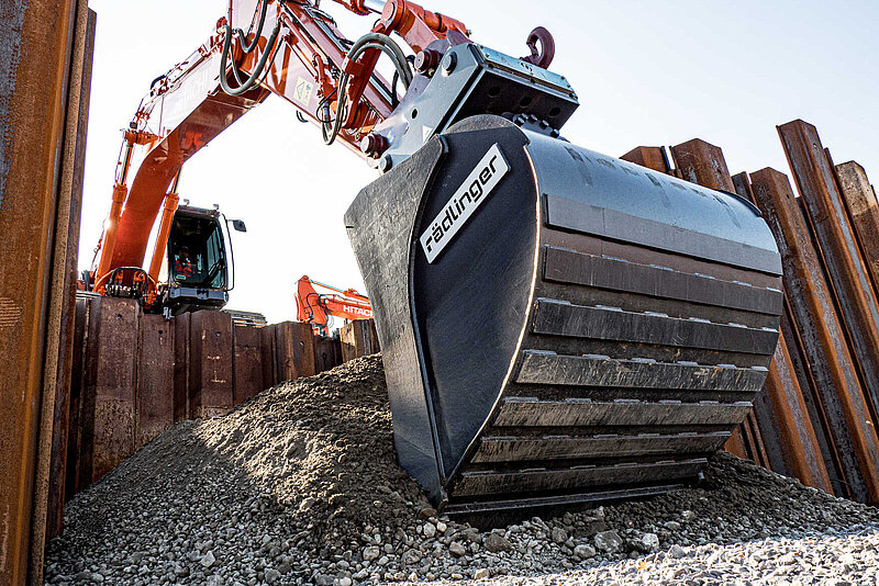 Backhoe Bucket with Tilt Motor picks up soil on a sheet pile wall